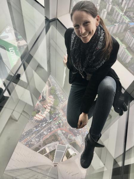 Photograph of Heather Fletcher sitting on the glass floor of a building in Seoul, South Korea.