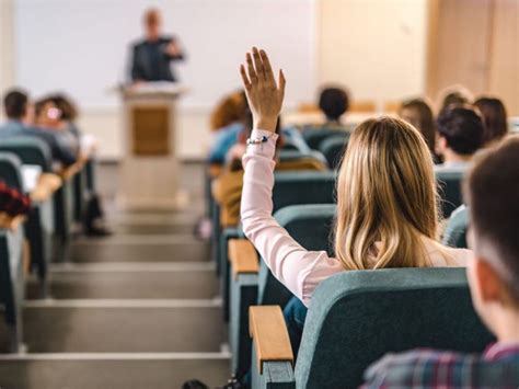 student raises her hand in a lecture hall